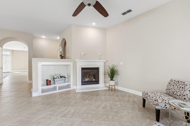 sitting room with light tile patterned floors, ceiling fan, visible vents, baseboards, and a glass covered fireplace