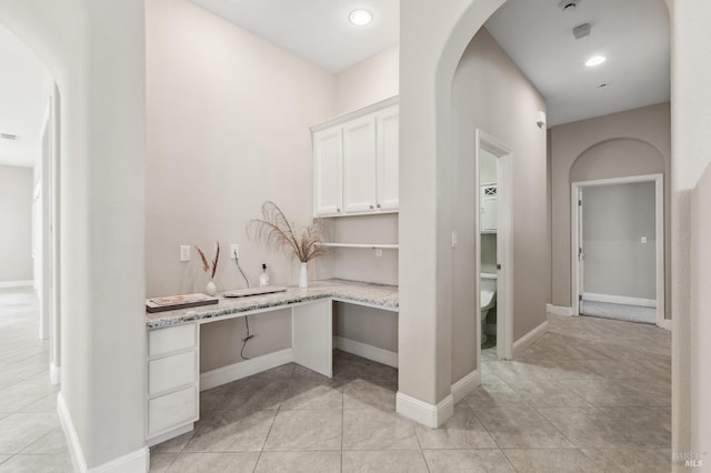 interior space featuring arched walkways, baseboards, and light tile patterned floors