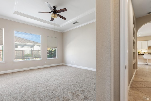 spare room with light carpet, visible vents, baseboards, a raised ceiling, and crown molding