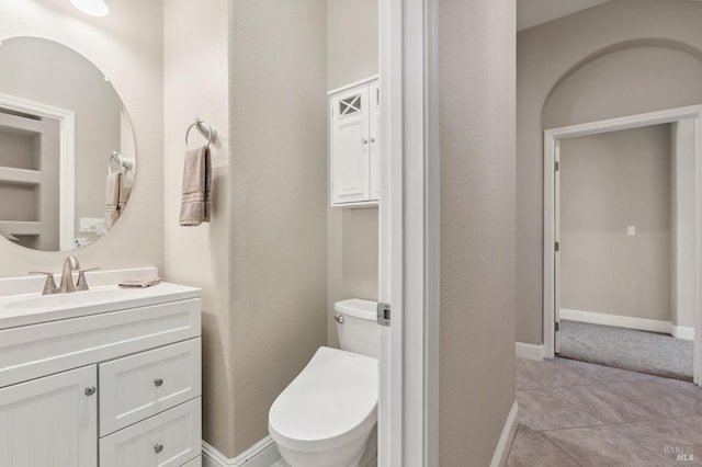 half bathroom with tile patterned flooring, baseboards, vanity, and toilet