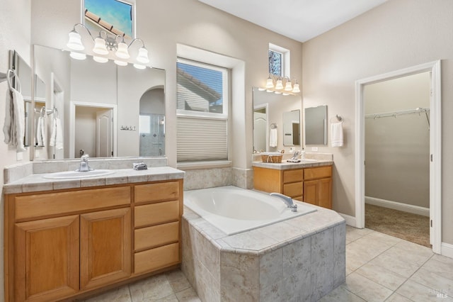 bathroom featuring a bath, a spacious closet, two vanities, and a sink