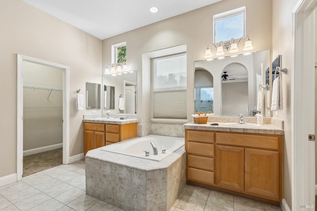 bathroom featuring a walk in closet, a garden tub, two vanities, and a sink