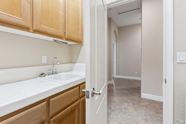 clothes washing area with arched walkways, a sink, baseboards, and light tile patterned floors