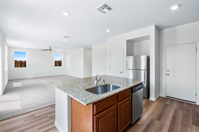 kitchen with light stone countertops, visible vents, a center island with sink, appliances with stainless steel finishes, and a sink