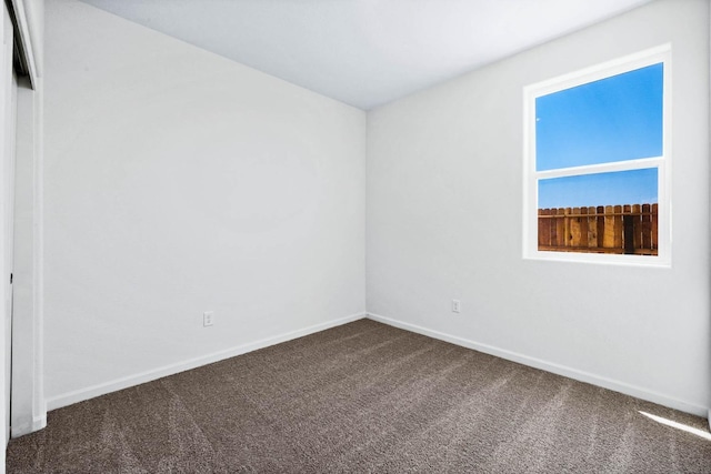 unfurnished room with dark colored carpet and baseboards