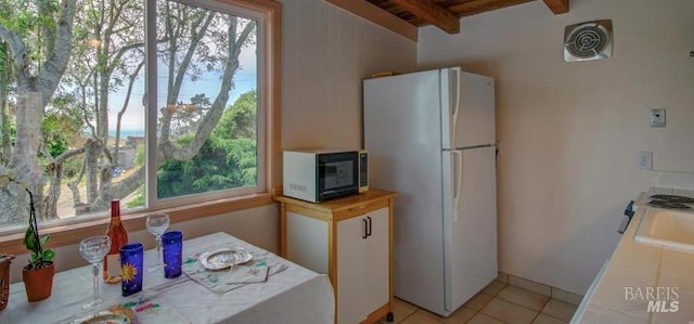 kitchen featuring freestanding refrigerator, black microwave, light countertops, and beam ceiling