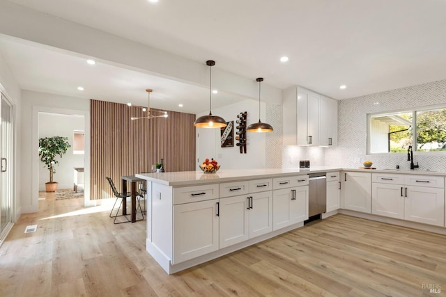 kitchen with light wood finished floors, a peninsula, white cabinetry, and a sink