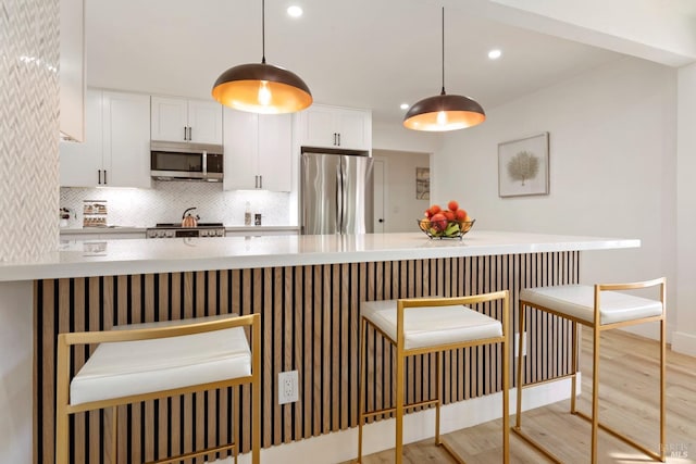 kitchen with wood finished floors, stainless steel appliances, light countertops, white cabinets, and backsplash