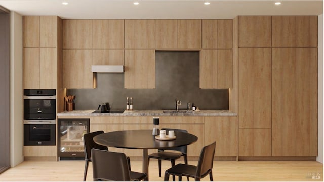 kitchen featuring under cabinet range hood, beverage cooler, double wall oven, light wood-style floors, and modern cabinets