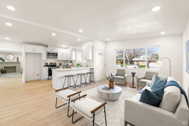 living room with light wood-style floors, baseboards, a fireplace with raised hearth, and recessed lighting