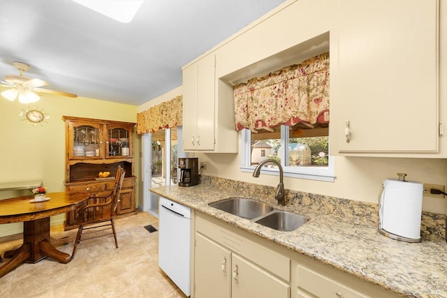 kitchen with a ceiling fan, white dishwasher, light stone counters, and a sink