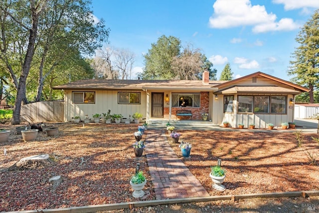 ranch-style home with board and batten siding, brick siding, a chimney, and fence