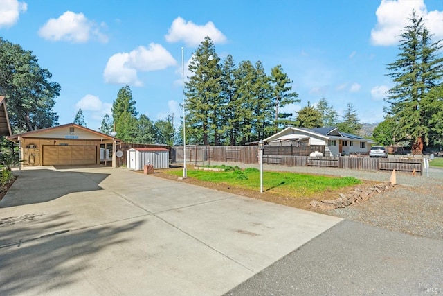 view of yard with driveway, a garage, an outbuilding, fence private yard, and a shed