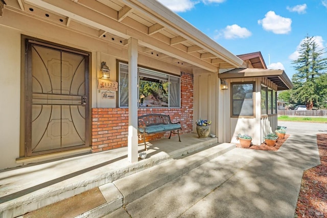 doorway to property with covered porch and brick siding