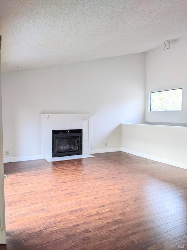 unfurnished living room with a textured ceiling, wood finished floors, a fireplace with flush hearth, and baseboards