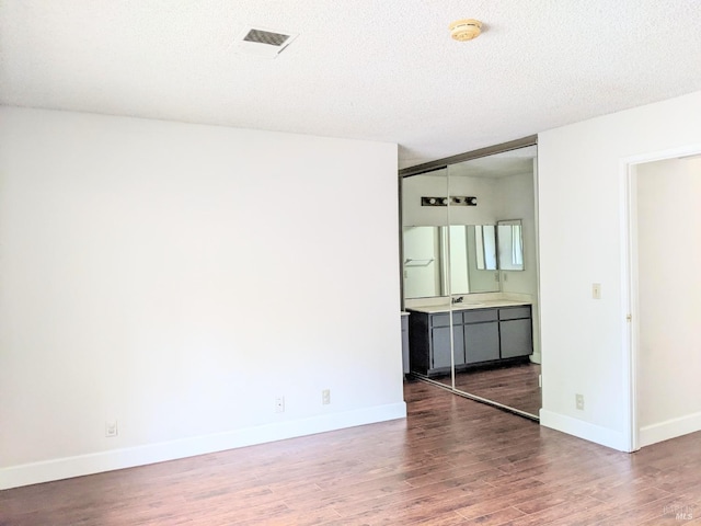 unfurnished bedroom with a textured ceiling, a sink, wood finished floors, visible vents, and baseboards