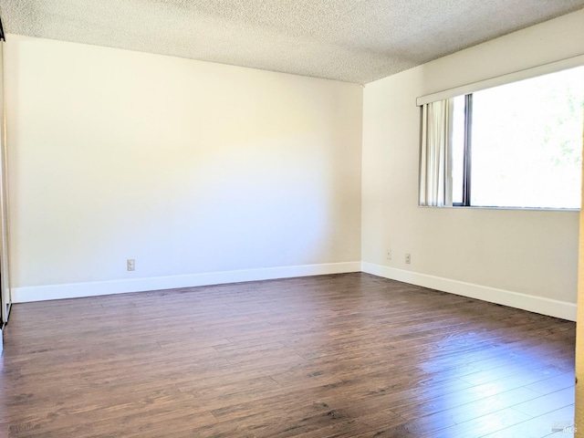 empty room with dark wood-style floors, a textured ceiling, and baseboards