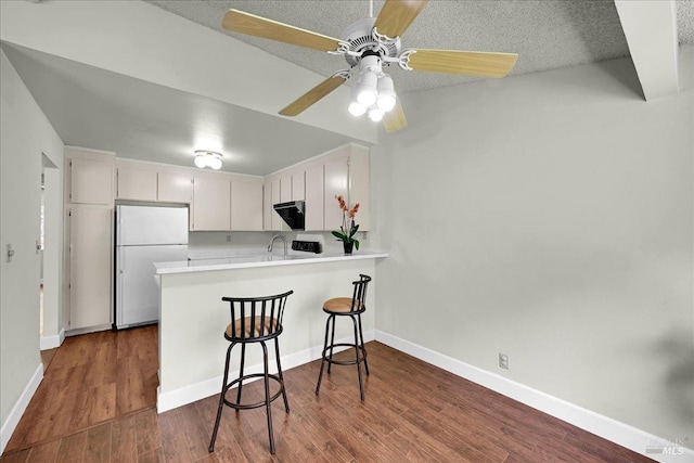 kitchen with white cabinets, light countertops, freestanding refrigerator, a ceiling fan, and a peninsula