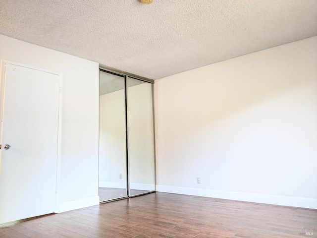 unfurnished bedroom with a textured ceiling, baseboards, and wood finished floors