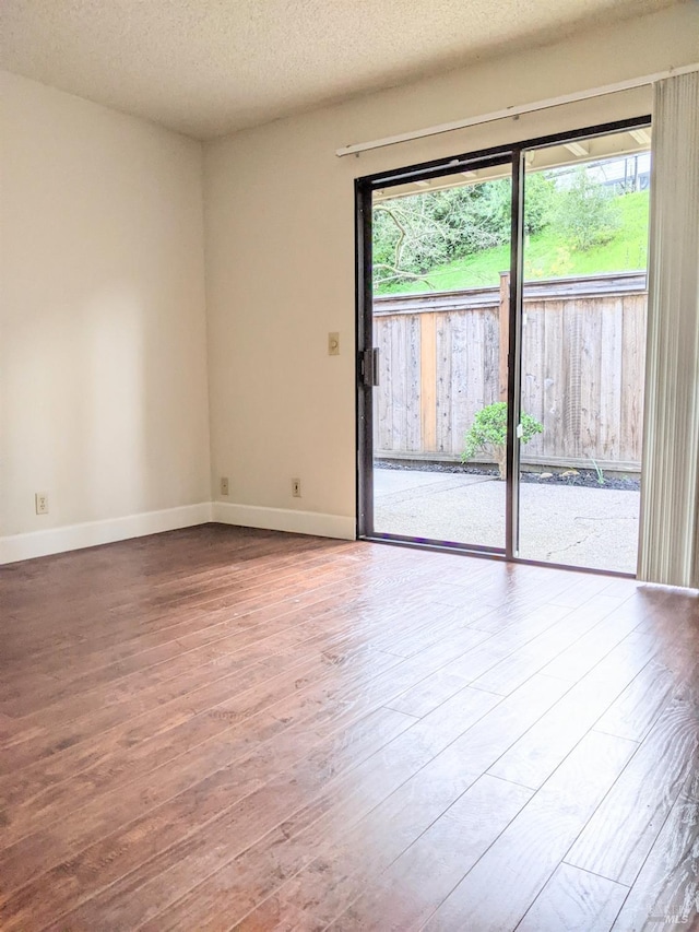 unfurnished room with plenty of natural light, a textured ceiling, baseboards, and wood finished floors