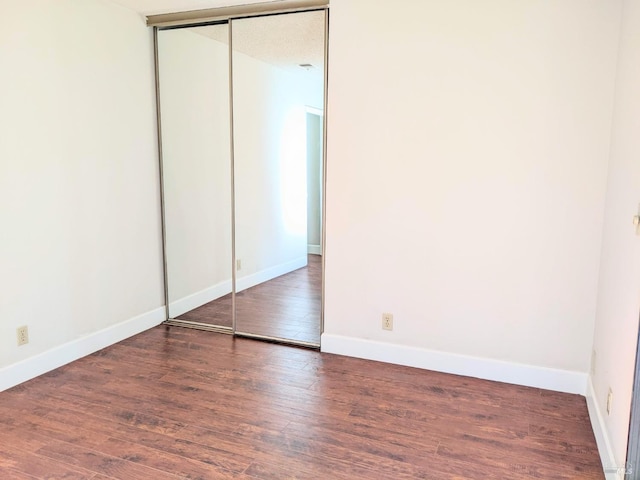 unfurnished bedroom featuring a closet, wood finished floors, and baseboards