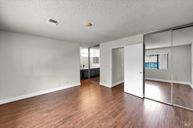 unfurnished bedroom featuring visible vents, dark wood-style flooring, a textured ceiling, and ensuite bathroom