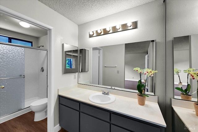 bathroom featuring toilet, wood finished floors, a textured ceiling, and a stall shower