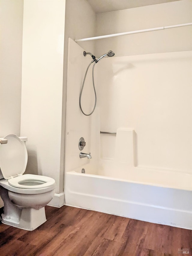 bathroom with bathtub / shower combination, toilet, and wood finished floors