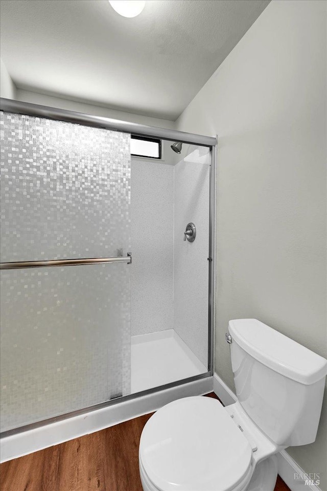 full bath with toilet, a stall shower, and wood finished floors