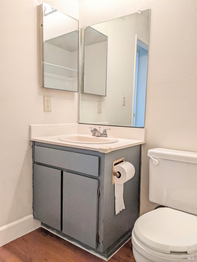 half bath with baseboards, vanity, toilet, and wood finished floors