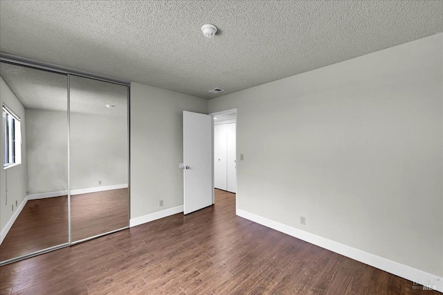 unfurnished bedroom with visible vents, baseboards, a closet, a textured ceiling, and wood finished floors