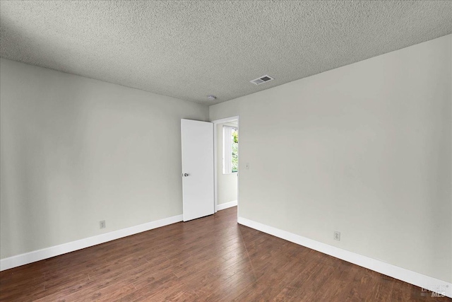 unfurnished room with a textured ceiling, baseboards, dark wood-style floors, and visible vents