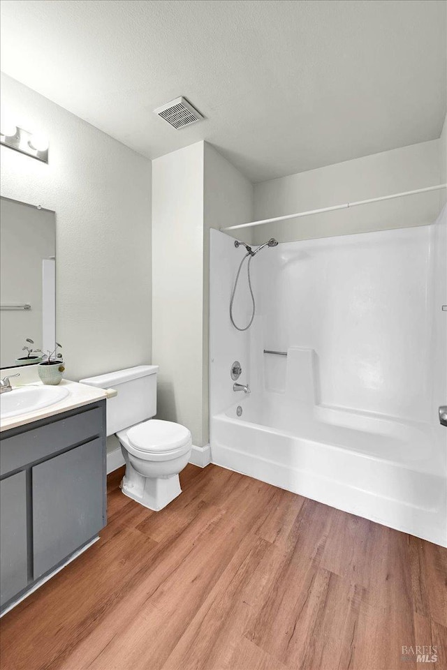 bathroom with visible vents, toilet, vanity, wood finished floors, and bathing tub / shower combination