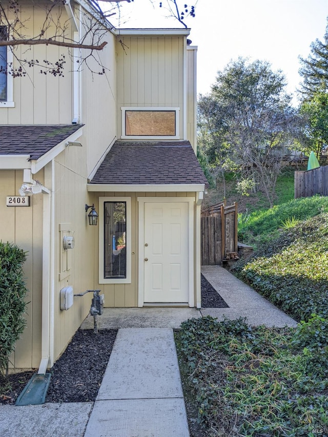 doorway to property featuring roof with shingles and fence