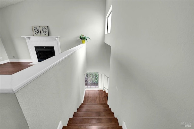 stairs with a fireplace with flush hearth, wood finished floors, a towering ceiling, and baseboards
