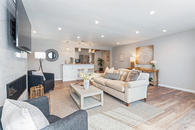 living area featuring light wood-style floors, baseboards, a tiled fireplace, and recessed lighting