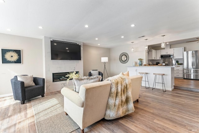 living room with recessed lighting, visible vents, a premium fireplace, light wood-type flooring, and baseboards