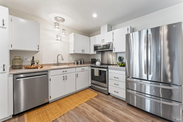 kitchen with decorative light fixtures, light countertops, stainless steel appliances, white cabinetry, and a sink