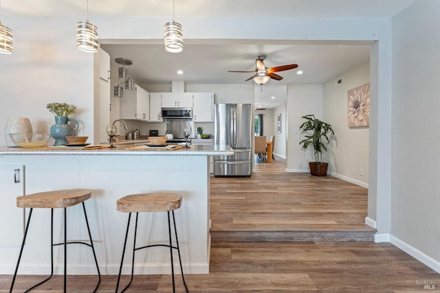 kitchen featuring decorative light fixtures, appliances with stainless steel finishes, white cabinets, wood finished floors, and a peninsula