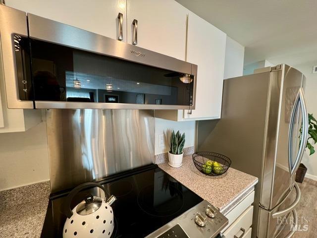 kitchen with stainless steel appliances, white cabinetry, and light stone countertops