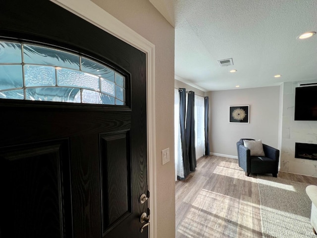 foyer entrance with a large fireplace, visible vents, a textured ceiling, light wood-type flooring, and recessed lighting