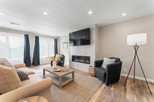 living room featuring recessed lighting, a fireplace, visible vents, baseboards, and light wood-style floors