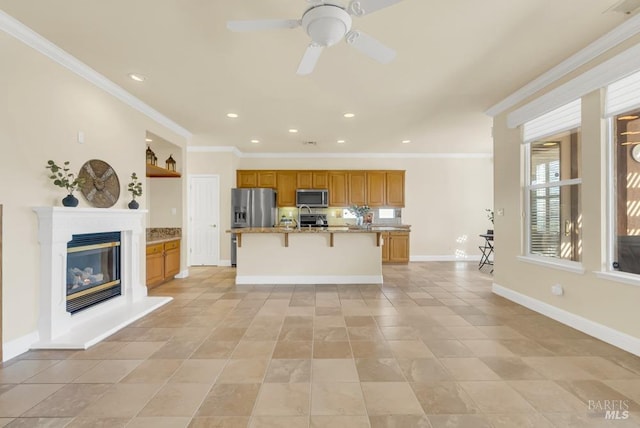 kitchen featuring crown molding, appliances with stainless steel finishes, a breakfast bar, brown cabinetry, and an island with sink