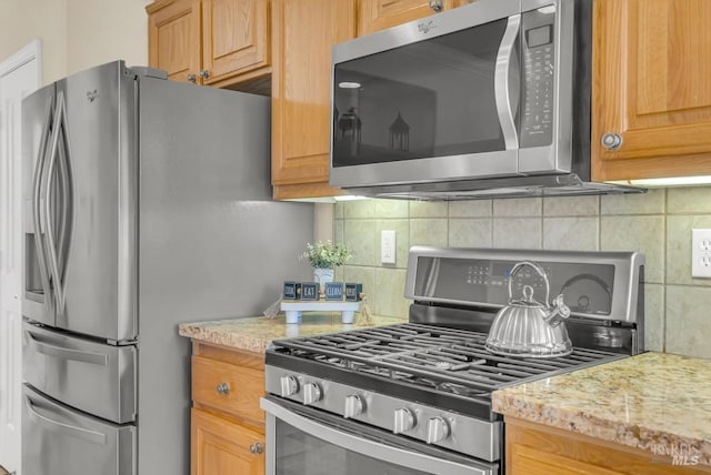 kitchen with appliances with stainless steel finishes, light stone countertops, and tasteful backsplash