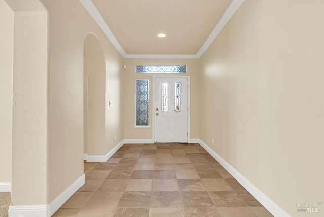 foyer entrance featuring arched walkways, ornamental molding, and baseboards