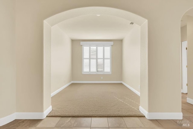 unfurnished room with baseboards, arched walkways, and light carpet
