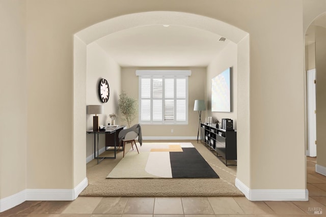 foyer with baseboards, arched walkways, and light colored carpet