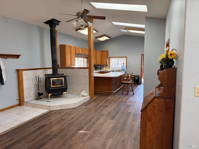 kitchen featuring brown cabinetry, lofted ceiling with skylight, stainless steel microwave, a wood stove, and light wood-style floors