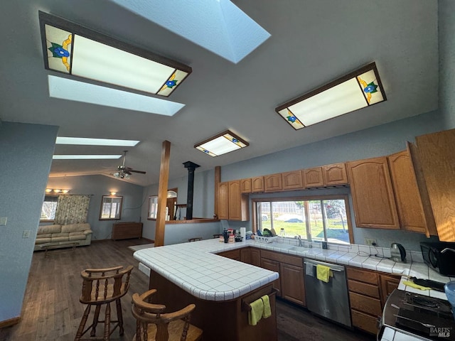 kitchen featuring vaulted ceiling with skylight, electric stove, tile countertops, a peninsula, and stainless steel dishwasher