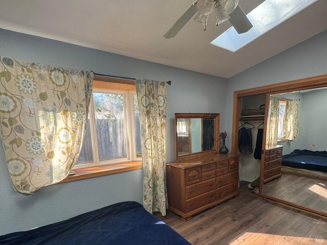 bedroom featuring vaulted ceiling with skylight, a closet, a ceiling fan, and wood finished floors